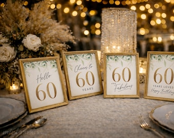 May include: Four rectangular gold-toned frames containing white cards with green watercolor leaf illustrations and gold text. The signs read Hello 60, Cheers to 60 Years, 60 and Fabulous, and 60 Years Loved Happy Birthday in elegant typography.