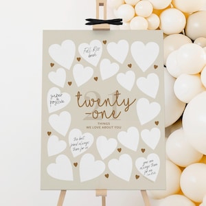 May include: A beige poster with white heart shapes for guests to write on. The poster has the text "twenty-one things we love about you".