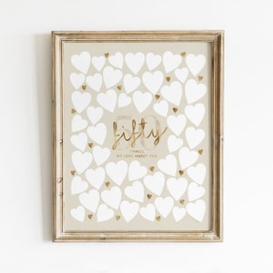 A beige poster with a gold frame. The poster has a gold inscription that says "fifty things we love about you". There are 50 white hearts on the poster.