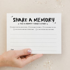 Puede incluir: Una tarjeta blanca con el texto "SHARE A MEMORY" en una fuente caprichosa. La tarjeta incluye indicaciones para compartir una historia, con líneas para escribir y casillas de verificación. La tarjeta está sostenida por una mano.