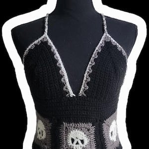 May include: Black crochet halter top with a V-neckline and skull accents. The top features a black base with gray and white skull motifs on the front. The straps and neckline are trimmed with a gray and white pattern.