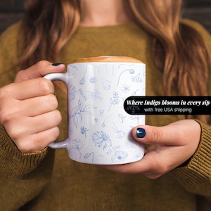 May include: White ceramic mug with a blue floral pattern and the text "Where Indigo blooms in every sip with free USA shipping". The mug has a handle and is filled with a brown liquid.