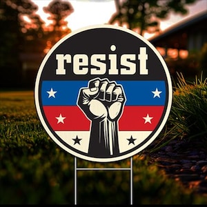 May include: A 24-inch diameter yard sign with the word "resist" in white letters on a black background. A raised fist with a red, white, and blue American flag design is in the center of the sign. The sign is made of corrugated plastic and includes a metal stake.