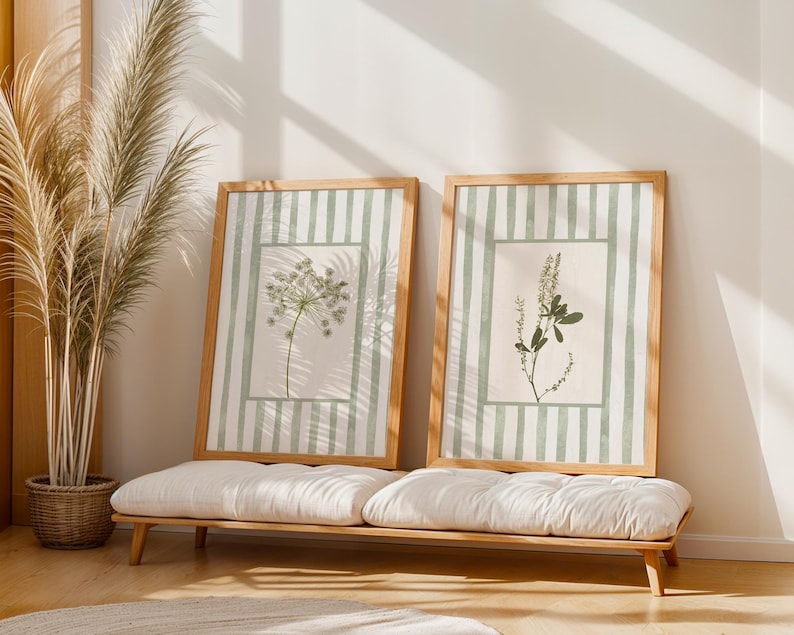 Peut inclure: Deux cadres avec des impressions botaniques sur fond ray&eacute; vert clair et des cadres en bois. Les impressions pr&eacute;sentent des illustrations de plantes d&eacute;licates. Elles sont expos&eacute;es sur un banc en bois avec des coussins blancs.