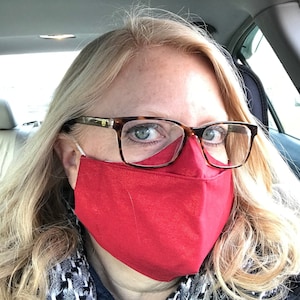 Może przedstawiać: Kobieta w czerwonej maseczce na twarz i brązowych okularach typu „żółw”. Maseczka jest wykonana z tkaniny i zakrywa nos i usta.