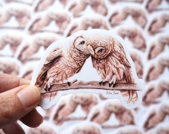 May include: A sticker featuring a watercolor illustration of two brown owls with their heads touching, perched on a branch. The sticker has a white background and the artist's signature "Faba Finch" is printed in the bottom right corner.