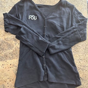 May include: A black long-sleeved cardigan with a button-up front and a small embroidered logo that says "PSU" on the left chest.