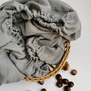 May include: A gray cotton muslin fabric sheet in a woven wicker basket with brown chestnuts scattered around it.