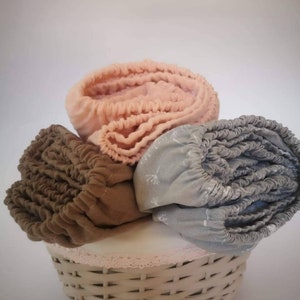May include: Three fabric diaper covers in a wicker basket. The covers are in shades of brown, peach, and gray. The basket has a white lining with a pink lace trim.