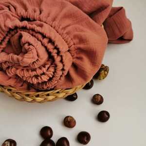 May include: A terracotta-colored muslin fabric swaddled in a basket with brown chestnuts scattered around it.