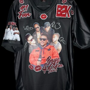May include: Black football jersey with a v-neck. The jersey features a graphic of a group of men, the text "Boys 4 Life Tour", and the text "#1 Fan". Red glitter accents include the letters "BBK" and lip shapes.