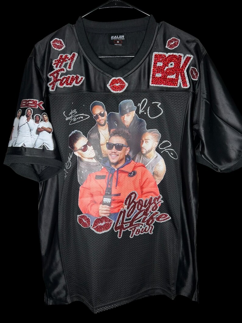 May include: Black football jersey with a v-neck. The jersey features a graphic of a group of men, the text "Boys 4 Life Tour", and the text "#1 Fan". Red glitter accents include the letters "BBK" and lip shapes.