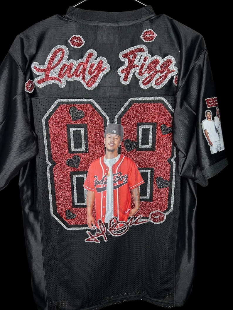 May include: Black baseball jersey featuring the name "Lady Fizz" in red glitter script. The number "88" is in red glitter with a photo of a person in the center. The jersey has a mesh design.