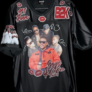 May include: Black mesh jersey with a V-neck, featuring a graphic of a group of men and the text "Boys 4 Life Tour." Embellished with red glitter accents, including the letters "B2K," lips, and the words "#1 Fan."