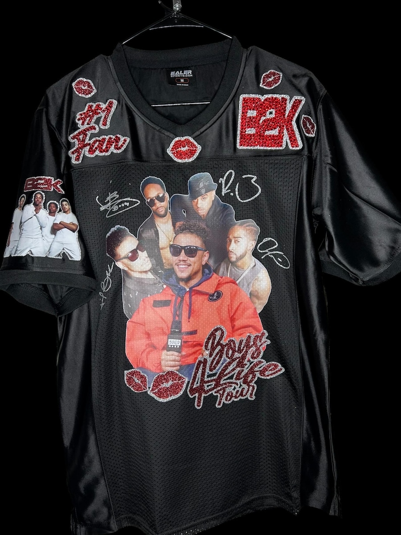 May include: Black mesh jersey with a V-neck, featuring a graphic of a group of men and the text "Boys 4 Life Tour." Embellished with red glitter accents, including the letters "B2K," lips, and the words "#1 Fan."