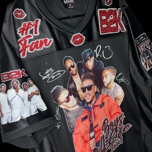 May include: Black jersey with a V-neck collar, featuring the text "#1 Fan" and "B2K" in red glitter. The jersey has images of a music group and the text "Boys 4 Life Tour".