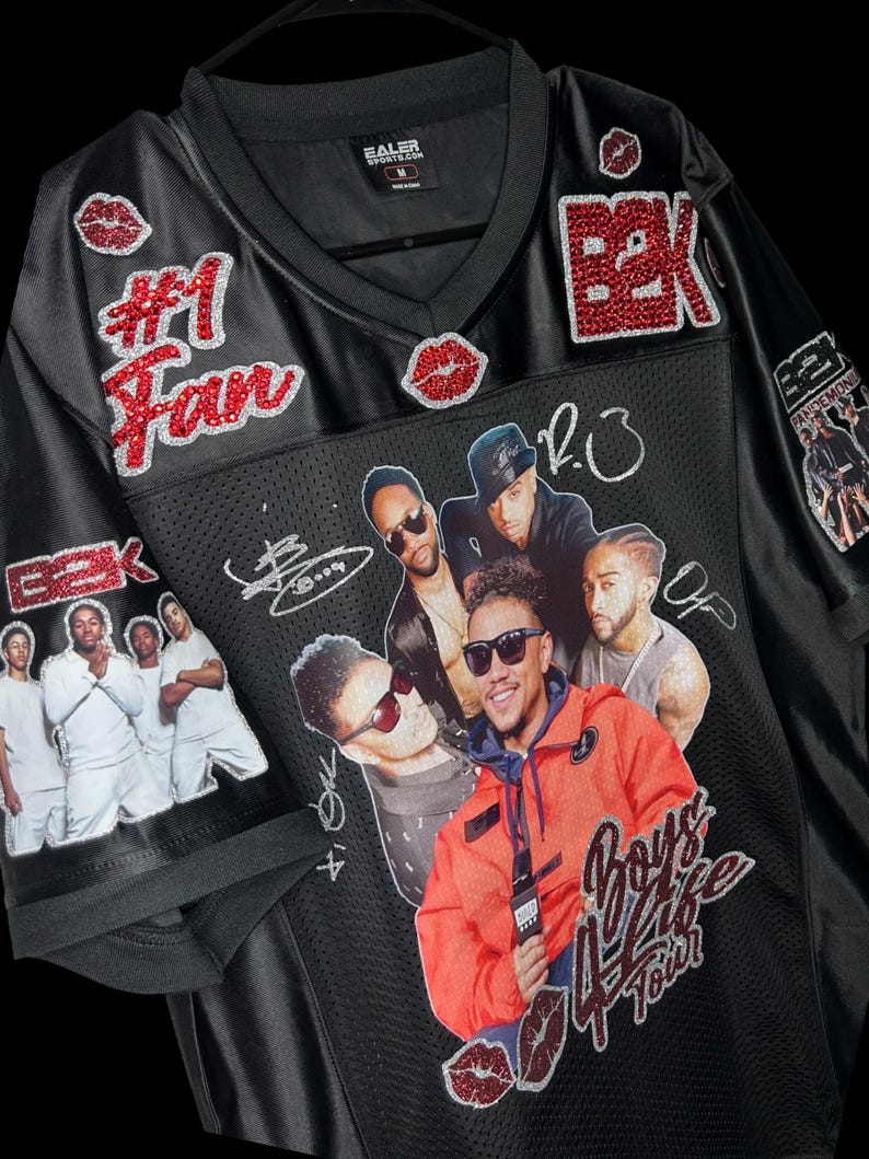 May include: Black jersey with a V-neck collar, featuring the text "#1 Fan" and "B2K" in red glitter. The jersey has images of a music group and the text "Boys 4 Life Tour".