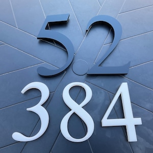 May include: Black and white house numbers, 52 and 384. The numbers are made of a thick, modern material and are mounted on a gray surface.