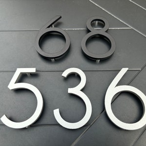 May include: Black and silver house numbers, 68 and 536, mounted on a gray surface.