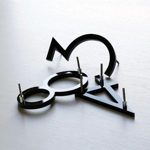May include: Black acrylic numbers, 3, 8, and a symbol, are arranged on a white surface. Each number has a small silver pin attached to the back.