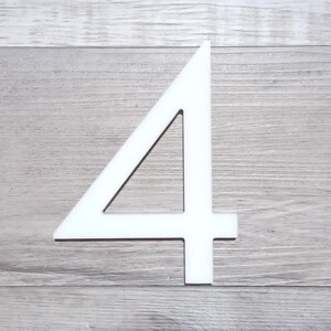 May include: White number four cutout, made of a thick material, against a woodgrain background.