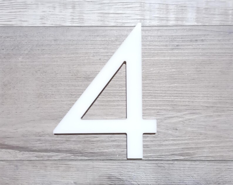 May include: White number four cutout, made of a thick material, against a woodgrain background.
