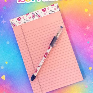 May include: Pink notepad with lined pages and a decorative border featuring hearts, syringes, and other medical-themed designs. A pen with a matching pattern rests on the notepad. The image includes the text "LCPrintsTN".