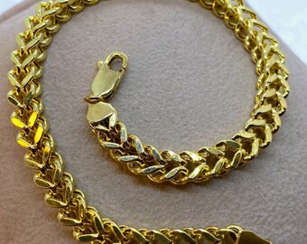 May include: A gold chain bracelet with a box clasp. The chain is made of interlocking links that form a braided pattern.
