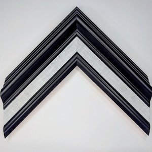 May include: A black picture frame with a white fabric insert, angled in a V-shape. The frame has a textured, layered design. The white fabric adds a contrasting element to the dark frame. Suitable for displaying photos or artwork.