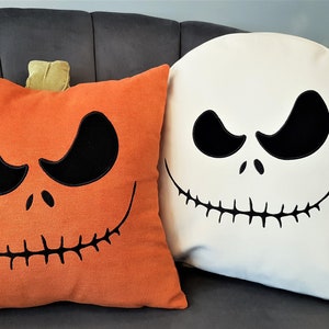 May include: Two Halloween themed throw pillows. One pillow is orange with a pumpkin face and the other is white with a Jack Skellington face.