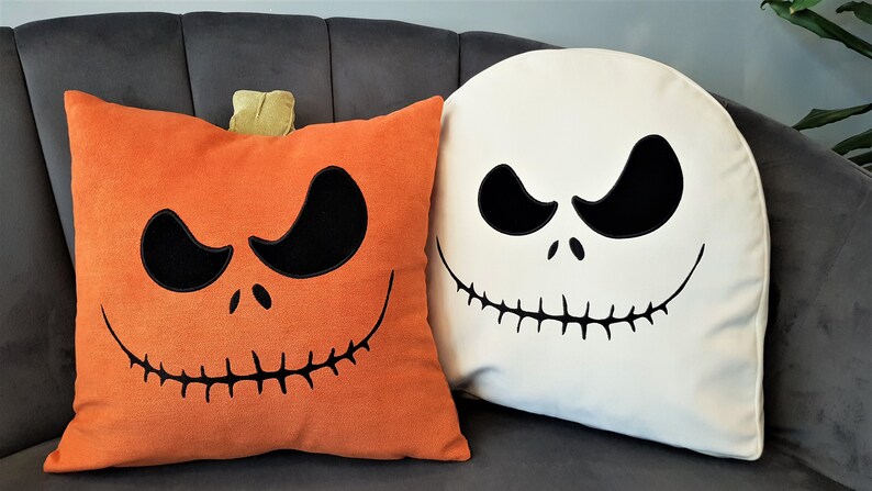 May include: Two Halloween themed throw pillows. One pillow is orange with a pumpkin face and the other is white with a Jack Skellington face.