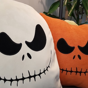 May include: Two Halloween-themed throw pillows. One is white with a black Jack Skellington face and the other is orange with a black pumpkin face.