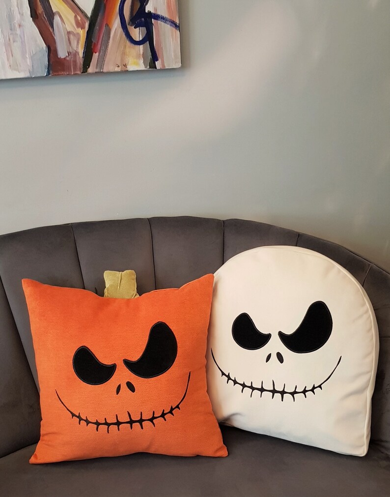 May include: Two Halloween themed throw pillows. One pillow is orange with a black Jack Skellington face. The other pillow is white with a black Jack Skellington face.