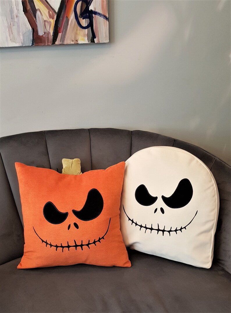 May include: Two Halloween themed throw pillows. One pillow is orange with a black Jack Skellington face and the other is white with a black Jack Skellington face.