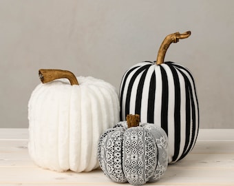 May include: Three decorative pumpkins, one white with a ribbed texture, one black and white striped, and one black and white with a lace pattern.