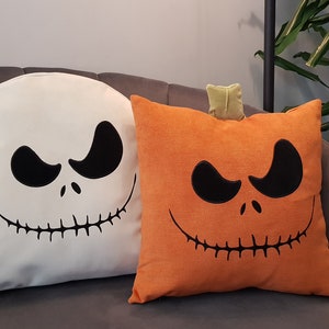 May include: Two Halloween themed throw pillows. One is white with a black Jack Skellington face and the other is orange with a black pumpkin face.