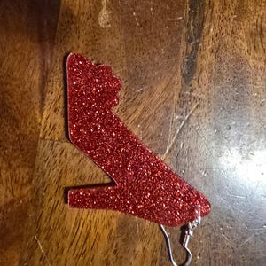 Puede incluir: Pendiente de zapato de tacón alto rojo con purpurina y gancho plateado.