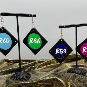 May include: Four pairs of earrings with different colored resin inserts. The earrings are black with silver and gold hooks. The resin inserts are blue, green, purple, and pink. The earrings are labeled with the numbers R60, R86, R59, and R339.