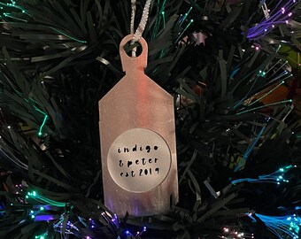 May include: Silver Christmas ornament with the text "indigo & peter est 2019" on a green artificial Christmas tree with colorful lights.