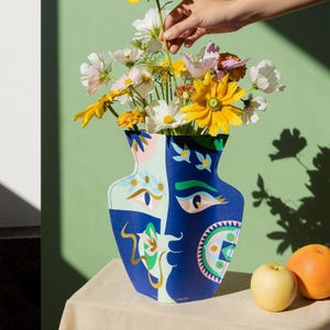 May include: A blue and white ceramic vase with a face design. The vase is filled with yellow, white, and pink flowers.