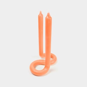May include: Two coral-colored candles are twisted into a unique shape, forming a loop at the base. The candles are made of a smooth, waxy material.