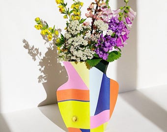 May include: A colorful geometric vase with a pink, orange, yellow, blue, and white design. The vase is filled with a bouquet of flowers, including purple, pink, and white flowers.