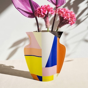 May include: A colorful geometric paper vase with a pink, yellow, blue, and orange design. The vase is filled with pink flowers and has the word "OCTAEVO" printed on the bottom.