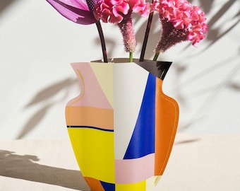 May include: A colorful geometric paper vase with a pink, yellow, blue, and orange design. The vase is filled with pink flowers and has the word "OCTAEVO" printed on the bottom.