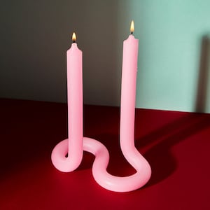 May include: Two pink candles in a unique, twisted design. The candles are lit and the wax is melting.