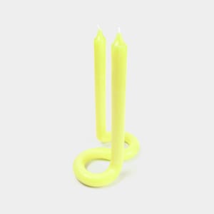 May include: Two yellow candles are connected in a unique, twisted design. The candles are tall and slender, with a smooth, glossy finish.