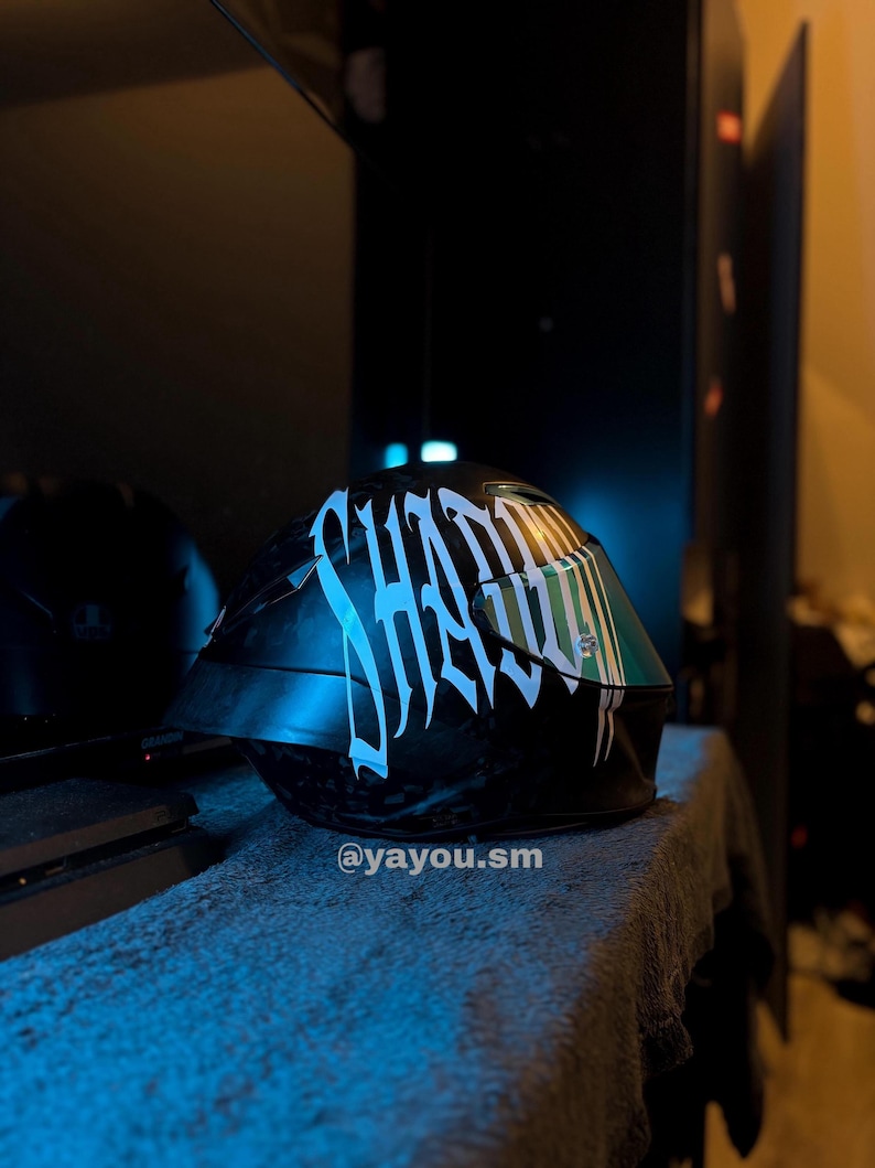 Puede incluir: Un casco de motocicleta negro con un texto gr&aacute;fico blanco grande y estilizado que dice SHADOW en el lateral. El casco tiene una visera oscura y reflectante e incluye el peque&ntilde;o texto blanco @yayou.sm impreso cerca del borde inferior.