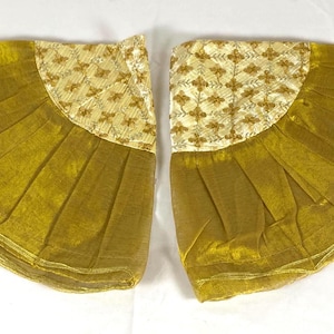 Puede incluir: Dos accesorios a juego en forma de abanico. La parte inferior es de tela plisada de color amarillo dorado. La parte superior es un panel semicircular con fondo crema y un motivo floral dorado repetido. Cada pieza tiene una pequeña borla.