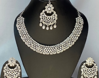 May include: A silver necklace and earrings set with a teardrop design and clear rhinestones. The necklace is on a black display stand.