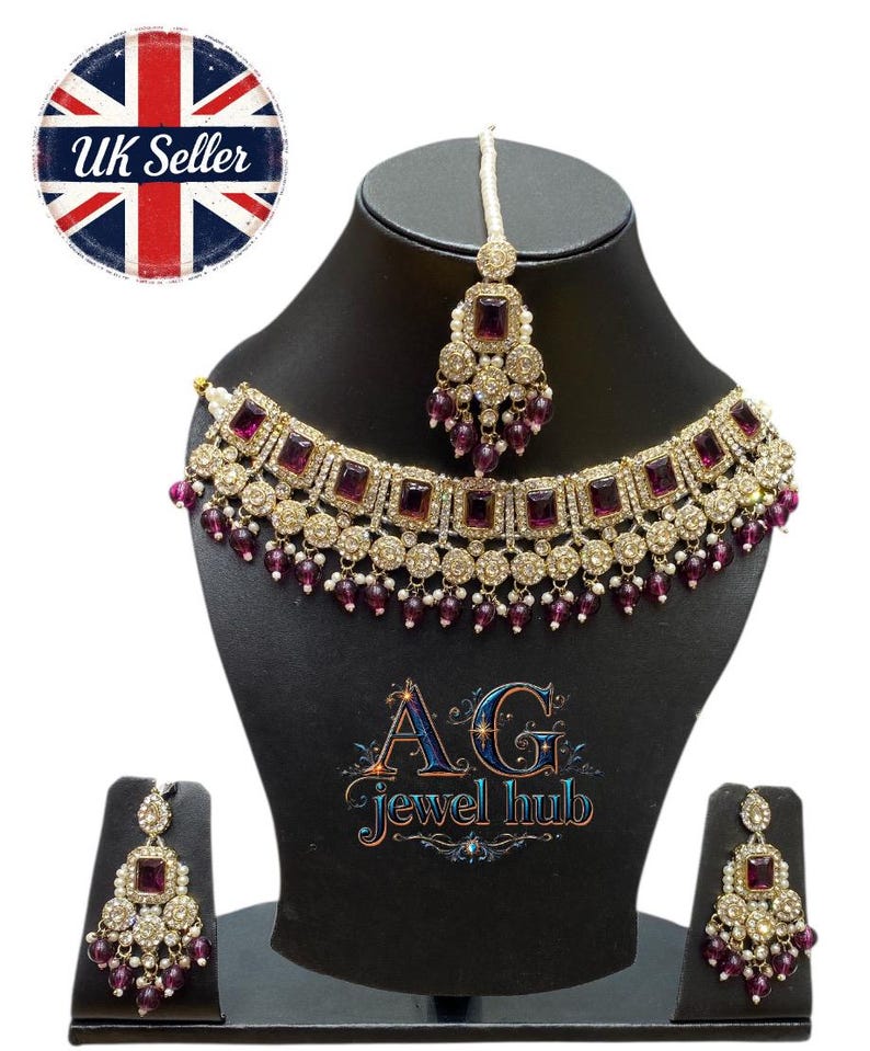 May include: A gold-toned necklace, earrings, and headpiece set with square, deep purple stones and small, dangling purple beads. The jewelry is displayed on a black mannequin head and stand. The set is from AG Jewel Hub, a UK seller.